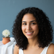 Smiling young adult woman with dark, curly hair, looking forward.